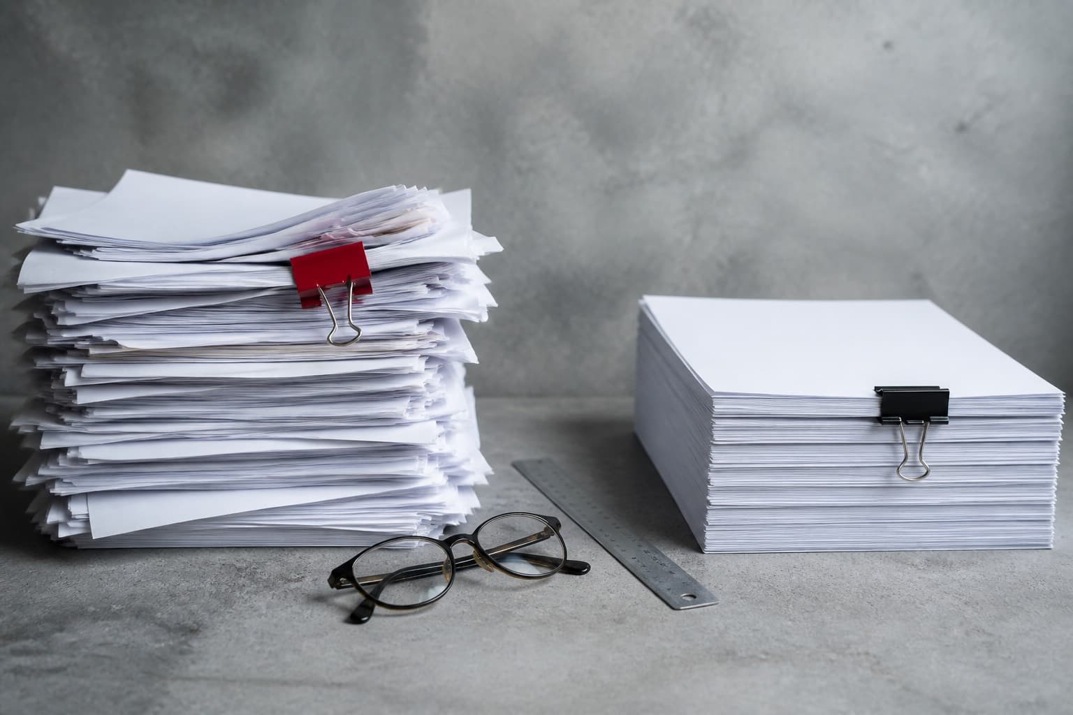 Two stacks of paper on a desk, one clipped and messy, one clipped and neat